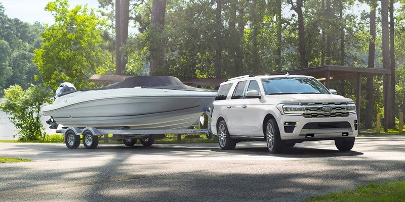 A white 2024 Ford Expedition towing a boat in a wooded area.