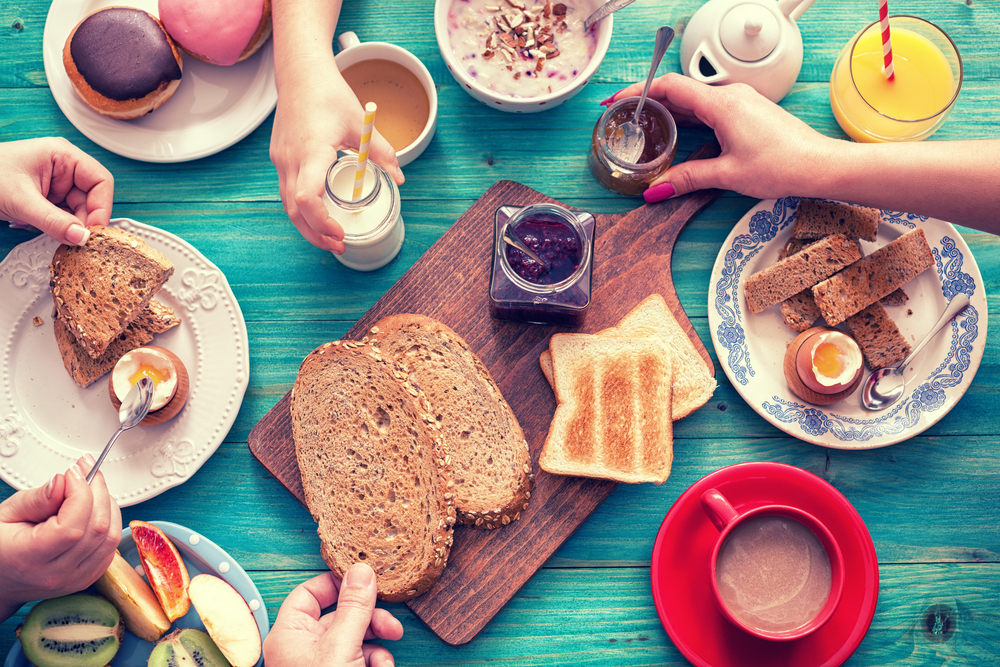 A table with breakfast foods and people reaching for them.