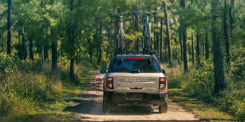A photo of the back of a 2024 Ford Bronco sport driving through a forest with bikes on top of the SUV.