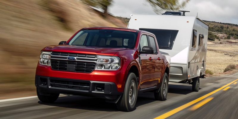 A red Ford Maverick towing a trailer down a highway.
